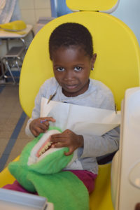 Juwany est assise sur un fauteuil jaune et joue avec une peluche de crocodile.